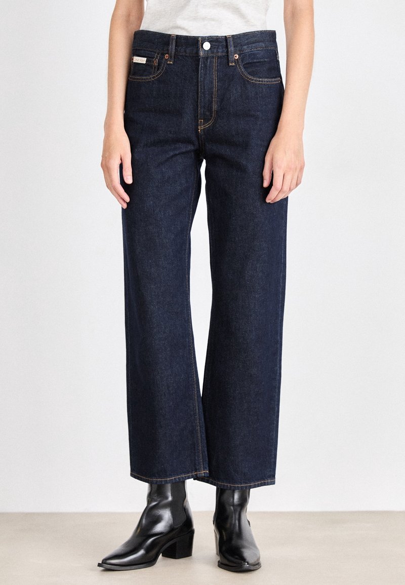 Mörkblå högmidjade vida jeans i denim, med kontrastsöm och framfickor. Bärs med svarta klackboots vid vristen.