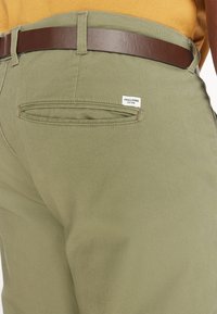 Olivno zeleni hlače iz bombaža, z zadnjo žepom, oznako z napisom "JACK & JONES" in dopolnjene s pravo usnjeno pasom v rjavi barvi.