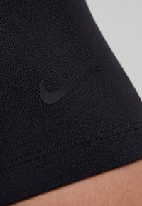 Tissu noir texturé avec un logo Nike swoosh noir près d'un ourlet cousu, porté près de la peau.