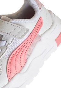 Sneaker bianca con accenti rosa, upper in pelle texturizzata e mesh, cinturino regolabile e suola bianca imbottita con un design del battistrada prominente.