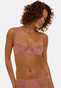 Soutien-gorge rose clair avec panneaux transparents et détails brodés en rose foncé. Modèle avec armatures, bretelles réglables et bonnets sans coutures.