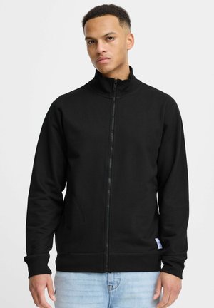 Sweatshirt noir zippé avec un col montant, des manches longues, des poches latérales et une petite étiquette logo près de l'ourlet. Tissu doux avec une texture lisse.