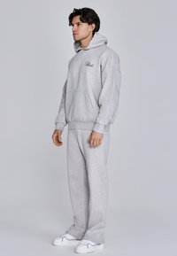 Gray hoodie with kangaroo pocket and text logo. Paired with matching loose-fit gray sweatpants. Both made of soft cotton blend fabric.