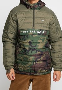 Grøn og brun camouflage dunjakke med en halv lynlås, med stor "OFF THE WALL" tekst på forsiden og justerbar hætte.