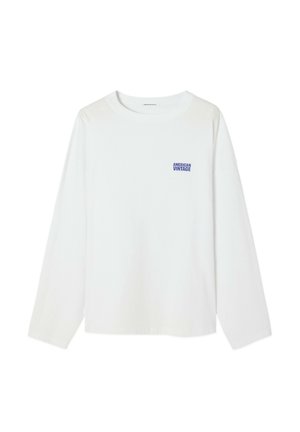 Balta ilgomis rankovėmis medvilninė marškinėliai, su mažo mėlyno "American Vintage" logotipo ant krūtinės, apvalia iškirpte ir laisvu siluetu.