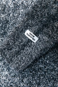 Lesklá kovová strieborná tkanina s hustými vláknami, na ktorej je biela nálepka s nápisom "COLOURFUL REBEL."