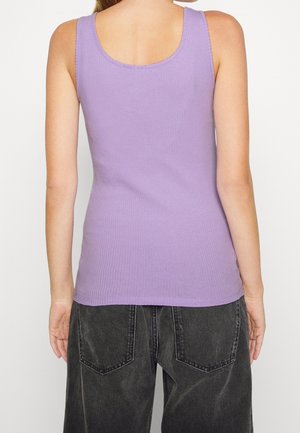 Person iført en ærmeløs, ribbet lavendelfarvet top og løse sorte denimbukser, vist fra ryggen mod en ensfarvet baggrund.