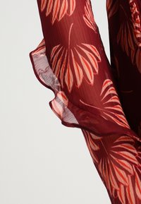 Tissu transparent bordeaux avec un motif floral en crème et corail. Présente des bords froncés et une texture légère, idéal pour superposer.