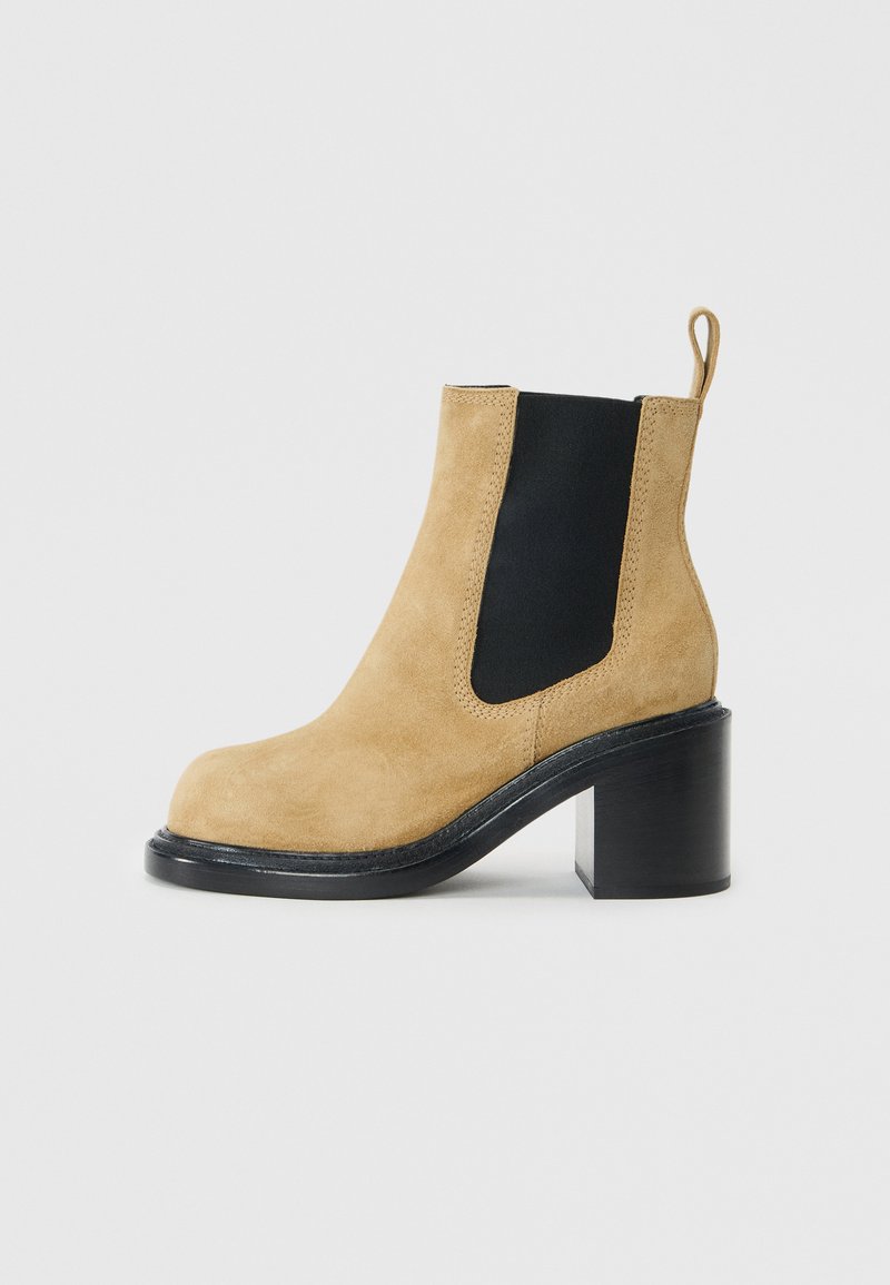Semišové kotníkové boty v béžové barvě s černým elastickým bočním panelem, kulatou špičkou a masivním černým podpatkem, s poutkem na zadní straně.