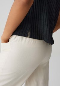 Top in tessuto nero a costine con fessure laterali, abbinato a pantaloni crema leggeri e dalla texture morbida con tasca laterale.