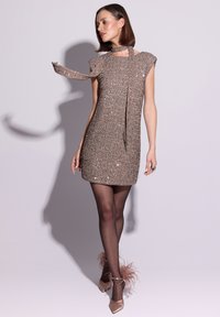Błyszcząca mini sukienka w kolorze różowego złota z krótkimi rękawami typu cap, wiązaniem przy szyi i zdobionym wzorem. Dobraną do niej cielistą pończochą i butami z piórami.