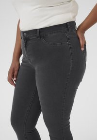 Vaqueros de denim gris oscuro, ajustados, con una cintura de altura media, que cuentan con bolsillos frontales y costuras sutiles. El material es suave con un ligero estiramiento.