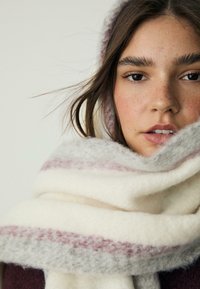 Sciarpa di lana bianca e grigia con una texture morbida, caratterizzata da una striscia orizzontale rosa. Sciarpa stilizzata attorno al collo, sovrapposta per calore.