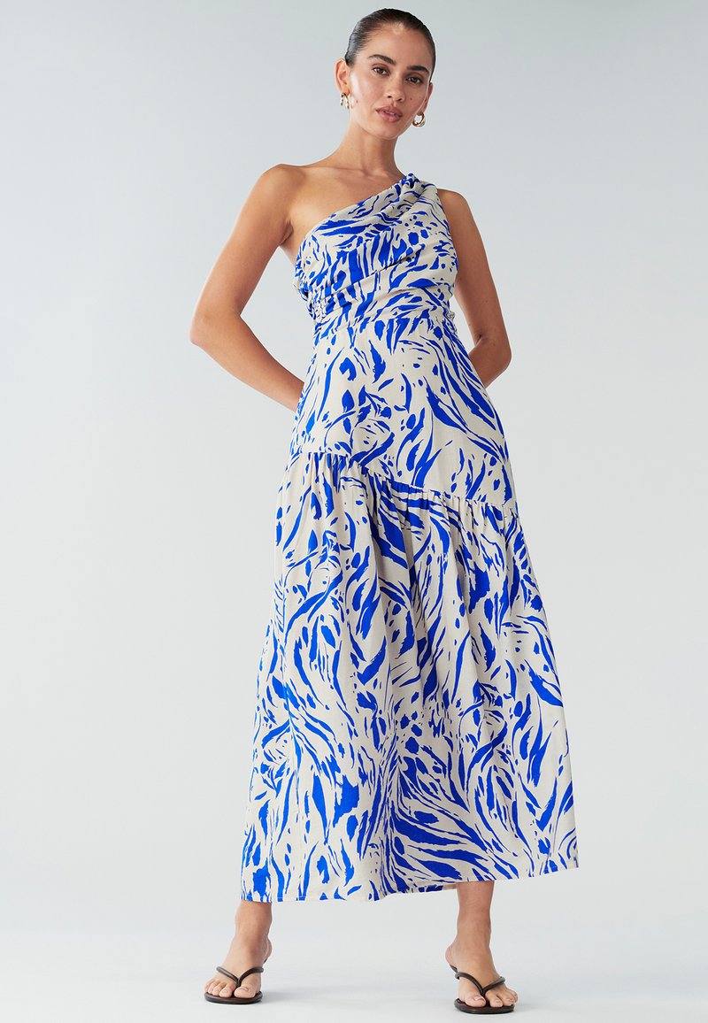 Robe longue asymétrique avec une épaule dégagée, présentant un motif abstrait bleu et blanc, un tissu froncé au niveau de la poitrine, et une jupe fluide. Texture douce, tissu léger.