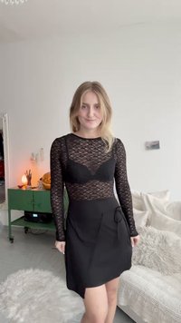 Top din dantelă neagră cu mâneci lungi, stratificat peste o rochie neagră fără bretele, cu un design înfășurat și detalii cu nod lateral. Textură netedă și formă ajustată.