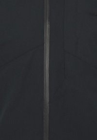 Sort jakke med en fremtrædende lynlås, vinklet sømme og en glat overflade. Minimalistisk design uden synlige logoer eller pynt.