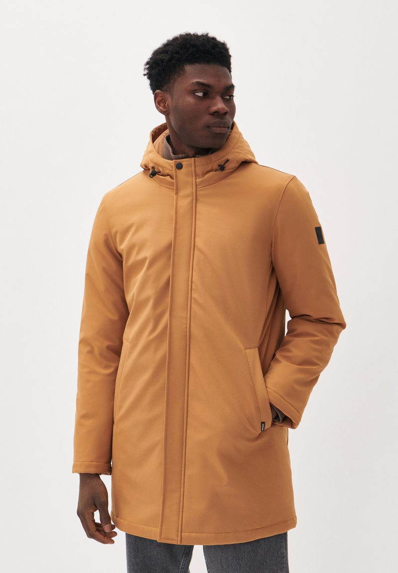Parka impermeable de color marrón claro fabricada con un material suave. Cuenta con una capucha, cierre de cremallera, bolsillos laterales y un acento negro en la manga.