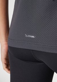 T-shirt de sport gris en tissu texturé avec le logo ClimaCool. Le t-shirt présente un design ajusté, des manches courtes et un ourlet arrondi, associé à des leggings noirs.