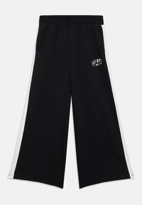 Crne široke hlače s bijelim bočnim trakama, elastičnim pojasom i logom "GAP NYC" na gornjoj lijevoj butini.