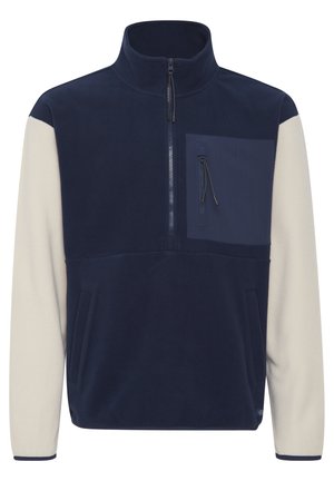 Pull en polaire bleu marine avec manches crème. Comprend un col zippé, des poches latérales et une poche sur la poitrine avec zip. Texture douce, design moderne.