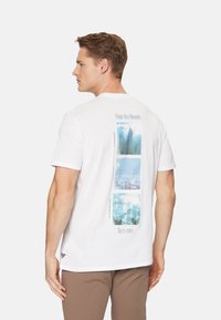 Camiseta de algodón blanca con un collage vertical de imágenes de paisajes urbanos en tonos azules en la espalda, con el texto: "Disfruta este momento" y "Aquí y ahora".
