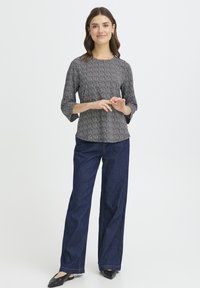 Sort og hvidt mønstret top med trekvartærmer, kombineret med mørkeblå bukser med vide ben. Sorte flade sko fuldender outfittet.