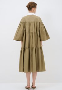 Vestito verde oliva, lunghi fino al ginocchio, con design a strati, maniche larghe e colletto bordato in pizzo bianco. Tessuto di cotone con consistenza liscia.