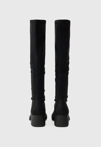 Μαύρες μπότες πάνω από το γόνατο με απαλό υφή, εφαρμοστή σχεδίαση, χοντρά τακούνια και χωρίς εμφανή μεταλλικά μέρη ή σχέδια.