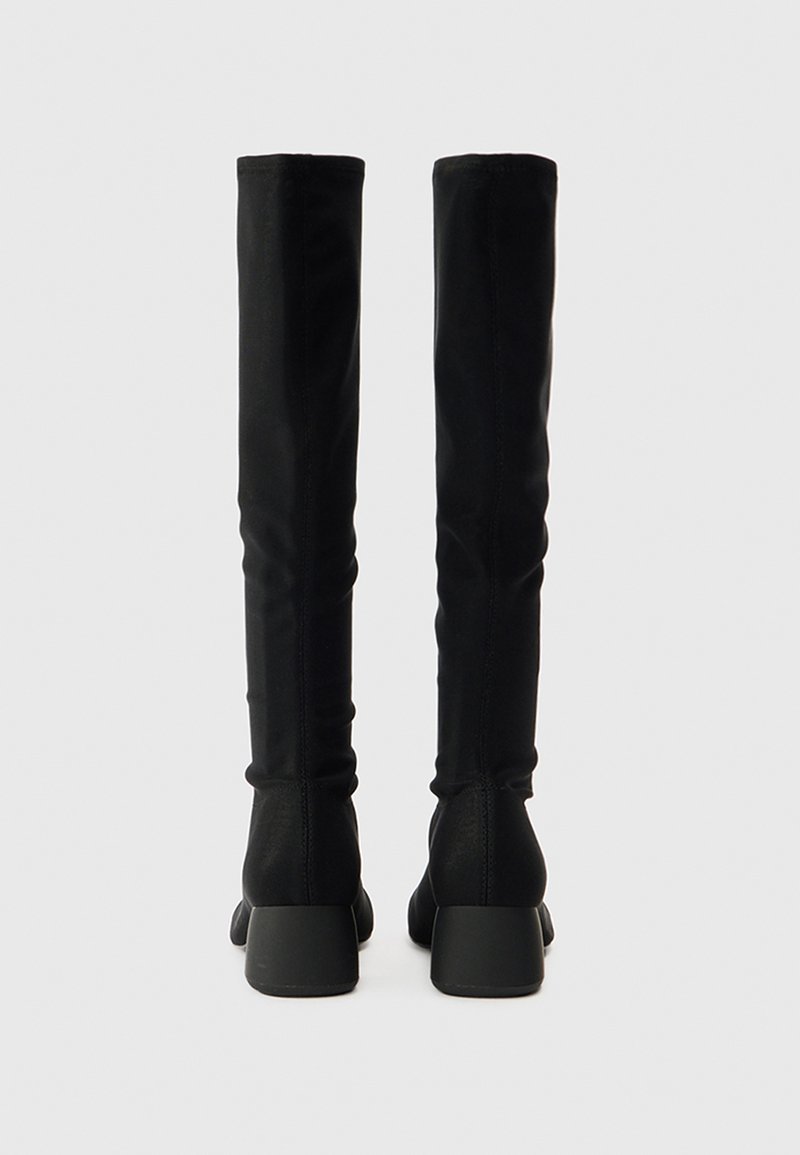 Schwarze Overknee-Stiefel mit glatter Oberfläche, körpernah geschnitten, mit klobigen Absätzen und ohne sichtbare Beschläge oder Muster.