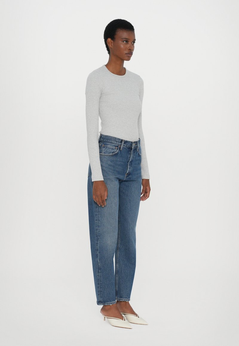 Light gray ribbed long-sleeve shirt paired with high-waisted blue denim jeans and white pointed-toe mules, standing on a white background.