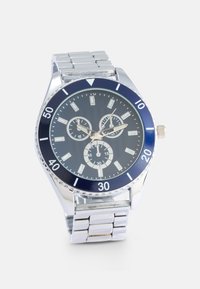 Orologio in acciaio inossidabile argentato con lunetta blu, quadrante scuro con texture, tre sottodial e indicatori delle ore luminescenti. Bracciale con maglie regolabili.