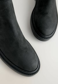 Mustad mustad ankle saapad ümarate varvastega ja tekstuurse pinnaga. Omavad kummist tallasid ja kontrastset õmblust äärtes.