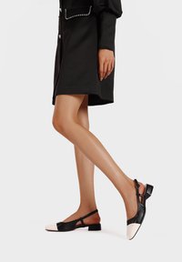 Scarpe slingback bianco e nero con tacco basso. Presentano una parte superiore in pelle nera e una punta in pelle bianca con un design arrotondato.