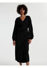 Schwarzes Wickelkleid aus weichem Stoff, mit langen Puffärmeln, einem tiefen V-Ausschnitt und dekorativen Knöpfen an der Seite. Einfaches und fließendes Design.