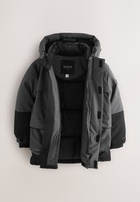 Isesoojustatud jakk erinevates hallides toonides, millel on kapuuts, eesmine lukk ja Velcro klapid. Valmistatud siledast, vastupidavast materjalist.