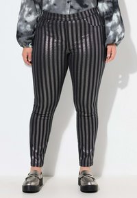 Pantalons rayés noirs et argentés avec une finition brillante, présentant une coupe slim et des poches discrètes, accompagnés de mocassins métalliques.