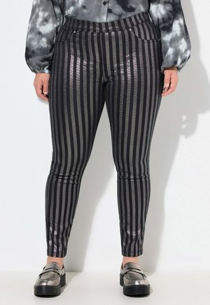 Pantalons rayés noirs et argentés avec une finition brillante, présentant une coupe slim et des poches discrètes, accompagnés de mocassins métalliques.