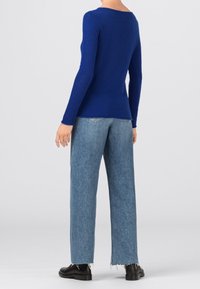 Pull tricoté bleu cobalt avec un léger col en V arrondi, associé à un jean large en denim clair et des bottines noires ornées de franges.