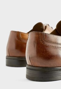 Zapatos de cuero marrón con un acabado suave, punta redonda, costuras detalladas y una suela de goma negra texturizada y baja. Enfócate en el tacón y la forma.