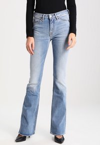 Bleka blå denim flared jeans med hög midja, fem fickor och en klassisk dragkedja. Bärs med en svart långärmad topp och klackskor.