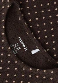 Bruine stof met gestructureerde strepen en beige polkadots. Label toont maatinformatie, met het "name it" logo zichtbaar. Zachte, gebreide textuur.