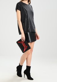 Czarna koszulka z krótkim rękawem ozdobiona srebrnymi ćwiekami, połączona z błyszczącą czarną mini spódnicą, czarnymi botkami sięgającymi do kostki oraz torebką na łańcuszku z czerwonymi akcentami.