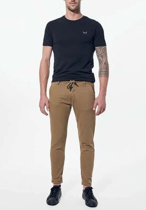 Sort kortærmet t-shirt med rund hals og lille logo; kaki chinos med snoretræk i taljen; sorte sko med tekstureret overflade.