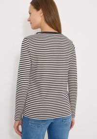 Haut à manches longues crème à rayures horizontales bleu marine, avec un col arrondi et une coupe décontractée, associé à un jean bleu.