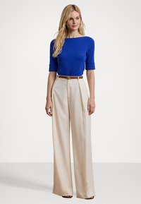 Blauwe korte mouwen top gecombineerd met crèmekleurige wijde broek, met een bruine riem met een gouden accent. Glad materiaal met een strakke pasvorm.