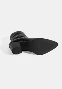 Bottine en cuir noir avec un talon épais, dotée d'une fermeture éclair latérale et d'une semelle en caoutchouc texturé. Surface supérieure lisse avec un minimum de détails.