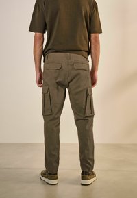 Olíva zöld pamut cargo nadrág, több oldalsó zsebbel és tapered lábformával. Sötét trikóval és sneaker cipővel viselve.