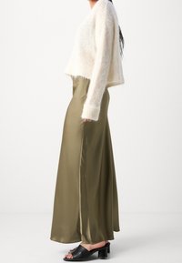 Pull en laine crème pelucheux superposé à une jupe maxi en satin olive, complété par des sandales à talons carrés noires. Contrastes de texture entre les matériaux.