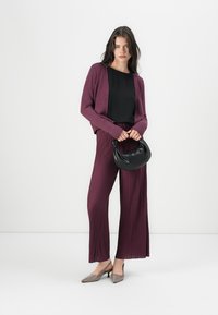 Burgundy cardigan over a black top, paired with pleated burgundy pants. Gray heels and a black handbag complete the outfit.