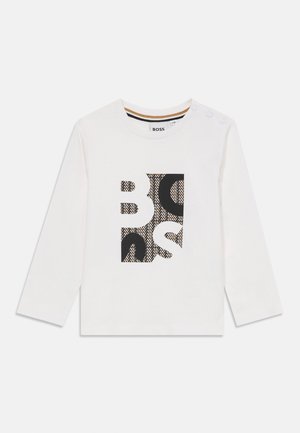 T-shirt blanc à manches longues avec un motif graphique noir et imprimé au centre, encolure ronde et trois boutons pression sur l'épaule.